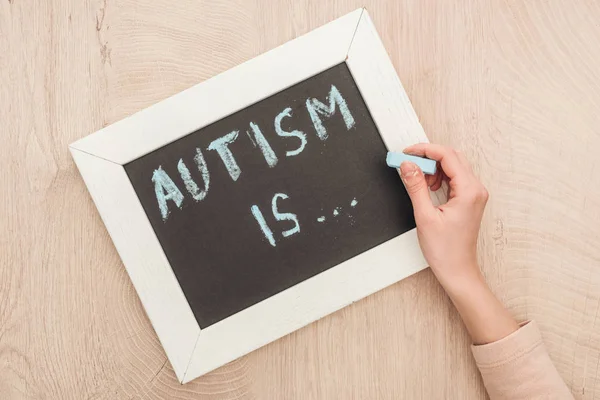 Partial view of woman writing autism is lettering with chalk on chalkboard — Stock Photo