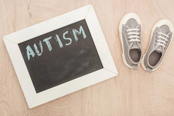 Вид надписи аутизма на доске рядом с детскими серыми кроссовками на деревянной поверхности — стоковое фото