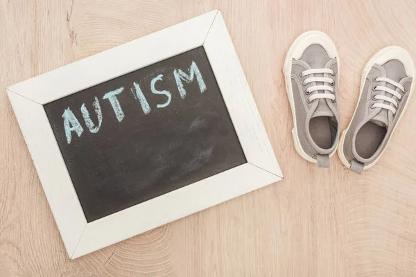 Vista superior de las letras autistas escritas en pizarra cerca de las zapatillas grises infantiles en la superficie de madera - foto de stock