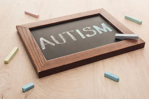 Iscrizione autistica scritta su lavagna tra gessetti sparsi multicolori su superficie lignea — Foto stock