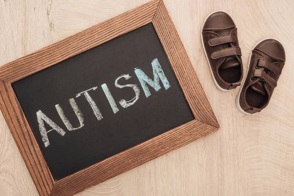 Vista superior de letras autistas escritas en pizarra cerca de las zapatillas marrones de los niños en la superficie de madera - foto de stock