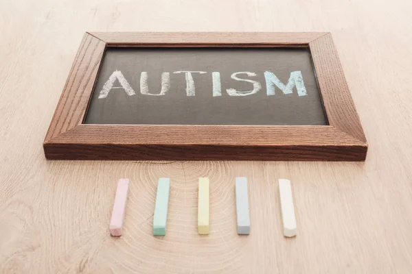 Autism lettering written on chalkboard near multicolored chalks on wooden surface — Stock Photo