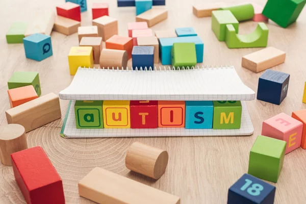 Autism lettering made of multicolored cubes in notebook among building blocks on wooden surface — Stock Photo