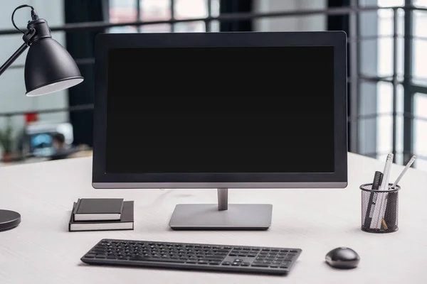 Monitor de computadora con pantalla en blanco y papelería en el lugar de trabajo en la oficina moderna - foto de stock