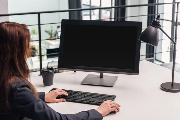 Cropped view of woman using computer at workplace with lamp and coffee to go in modern office — Stock Photo