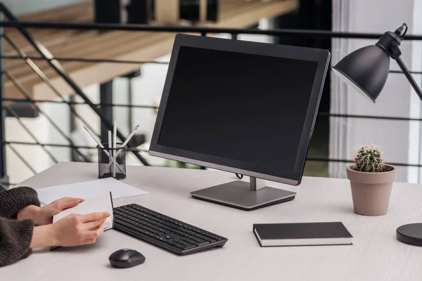 Visión parcial de la mujer sosteniendo portátil cerca de la computadora en el lugar de trabajo con artículos de papelería - foto de stock