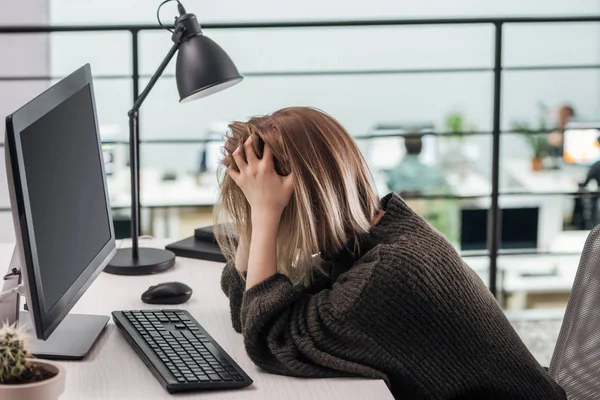 Депрессивная девушка сидит на рабочем месте с руками на голове в современном офисе — стоковое фото