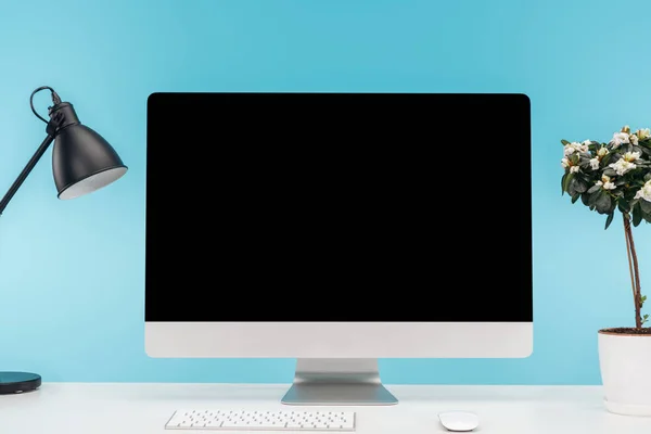 Lugar de trabajo con ordenador, lámpara y maceta sobre mesa blanca sobre fondo azul - foto de stock