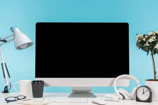 Lieu de travail avec ordinateur, lampe, tasse, café à emporter, calculatrice et écouteurs sur table blanche sur fond bleu — Photo de stock