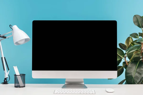 Lugar de trabajo con ordenador, lámpara, papelería sobre mesa blanca sobre fondo azul - foto de stock