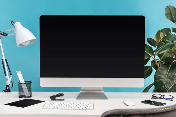Lugar de trabajo con gadgets, lámpara, papelería en la mesa blanca cerca de la planta verde sobre fondo azul — Stock Photo