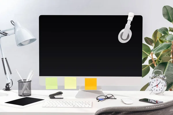 Posto di lavoro con cuffie e appunti adesivi vuoti su monitor, lampada e cancelleria su tavolo bianco su sfondo grigio — Foto stock
