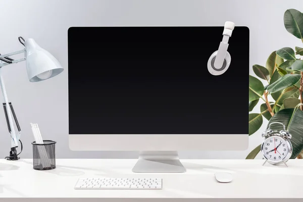 Arbeitsplatz mit Kopfhörer auf Computermonitor, Lampe und Schreibwaren auf weißem Tisch auf grauem Hintergrund — Stockfoto