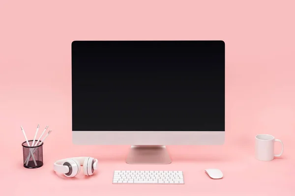 Рабочее место с компьютером, чашкой, наушниками и карандашами на розовом фоне — стоковое фото