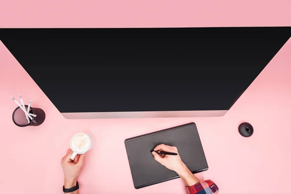 Partial view of man using graphic tablet and holding cup with coffee on pink background — Stock Photo