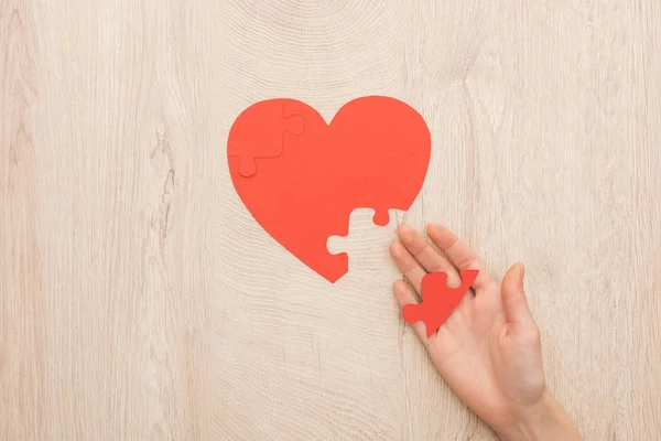 Vista recortada de la mujer sosteniendo rompecabezas del corazón sobre fondo de madera - foto de stock