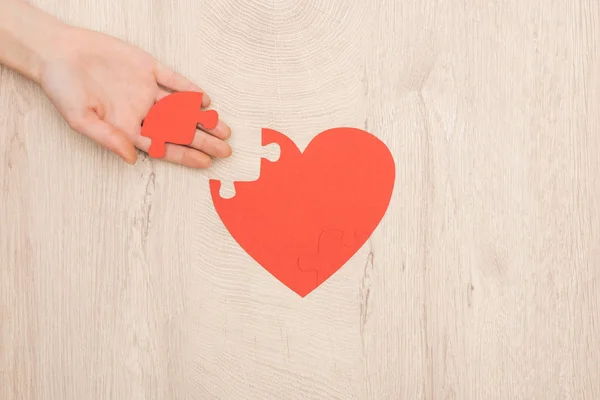 Vista parcial de la mujer sosteniendo rompecabezas del corazón sobre fondo de madera - foto de stock