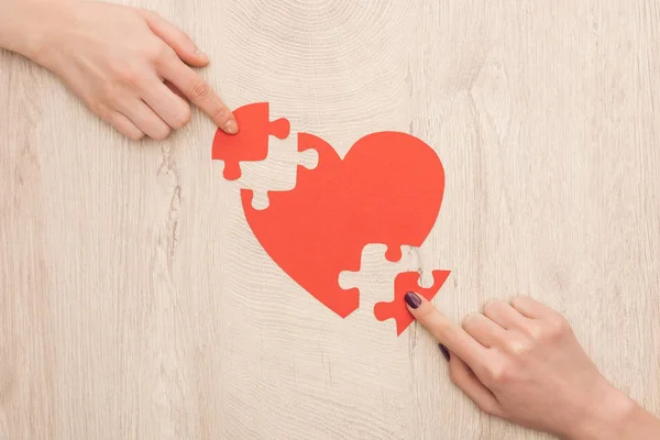 Обрезанный вид женщин, указывающих пальцами на кусочки головоломки и бумажного сердца — стоковое фото