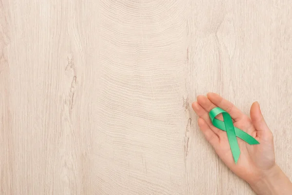 Cropped view of woman holding green ribbon on wooden background — Stock Photo