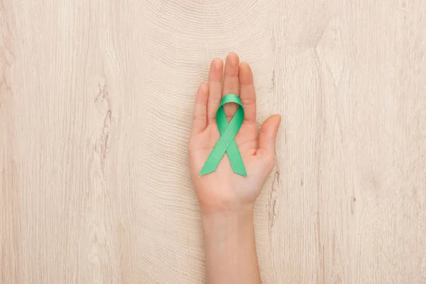 Partial view of woman holding green ribbon on wooden background — Stock Photo