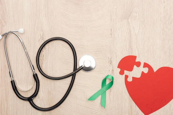 Vista dall'alto del cuore di carta, stetoscopio e nastro verde su sfondo di legno — Foto stock