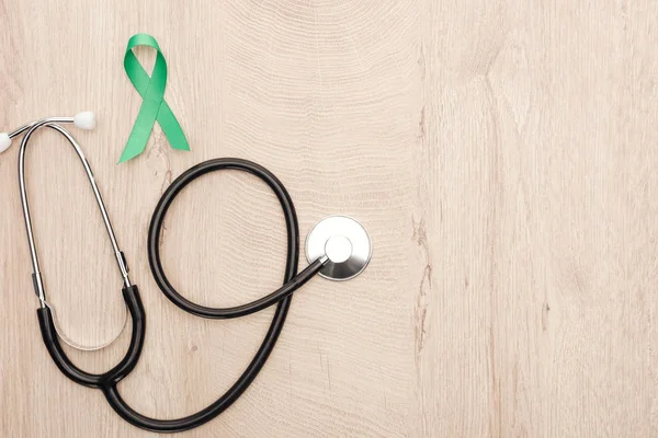 Top view of stethoscope and green ribbon on wooden background with copy space — Stock Photo