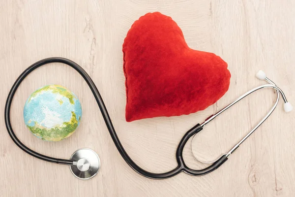 Vista dall'alto di cuore giocattolo luminoso e terra giocattolo, stetoscopio su sfondo di legno — Foto stock