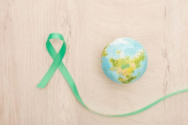 Top view of bright toy earth and green ribbon on wooden background — Stock Photo