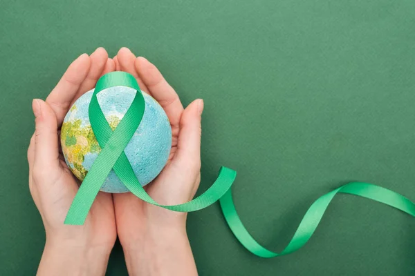 Partial view of woman holding toy earth and ribbon on green background with copy space — Stock Photo