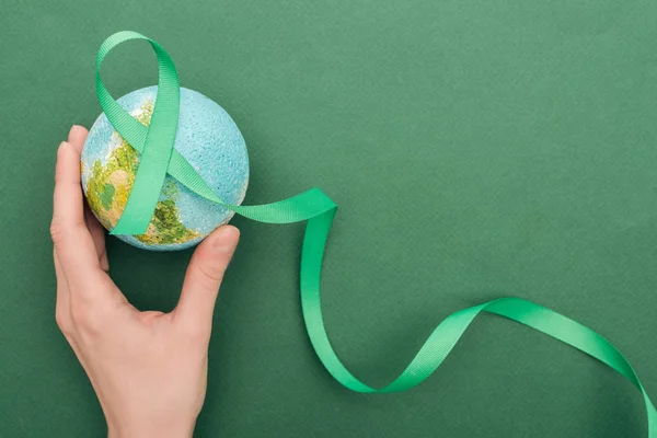 Cropped view of woman holding toy earth and ribbon on green background — Stock Photo