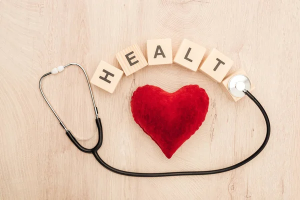 Vista superior de cubos con letras de salud, corazón de juguete y estetoscopio sobre fondo de madera - foto de stock