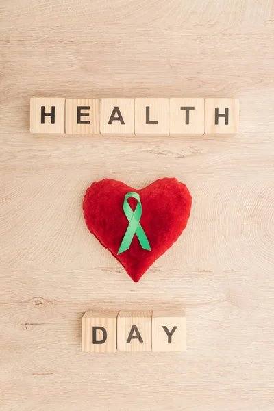 Top view of cubes with health day lettering, toy heart and green ribbon on wooden background — Stock Photo