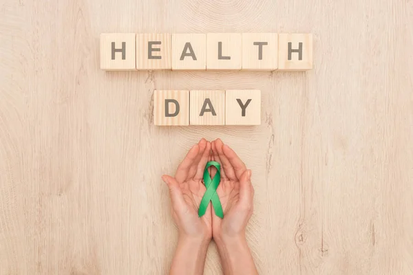 Vue du dessus de la femme tenant le ruban vert et les cubes avec le lettrage de jour de santé — Photo de stock