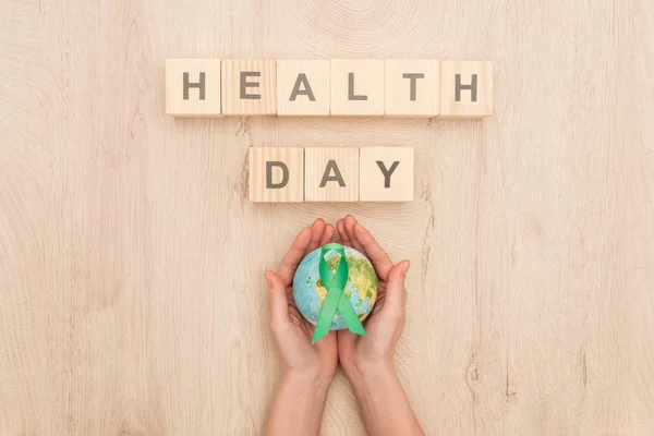 Вид зверху на жінку, що тримає іграшкову планету та зелену стрічку, кубики з написом на день здоров'я — стокове фото