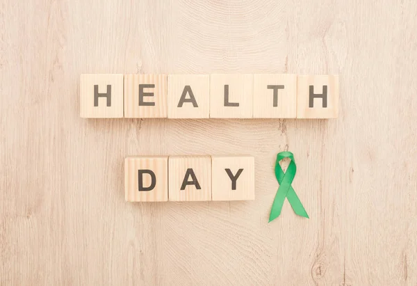Top view of cubes with health day lettering and green ribbon on wooden background — Stock Photo