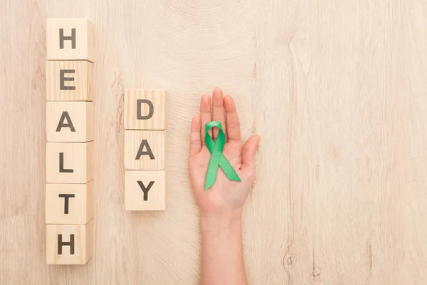 Vista recortada de la mujer sosteniendo cinta verde y cubos con letras del día de la salud — Stock Photo