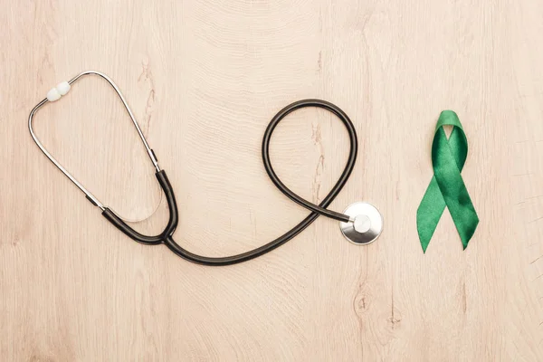 Top view of stethoscope and green ribbon on wooden background — Stock Photo