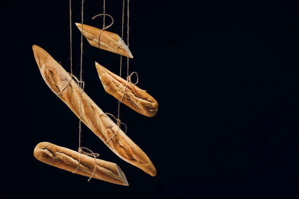 Loaves of fresh baked baguettes on ropes isolated on black — Stock Photo