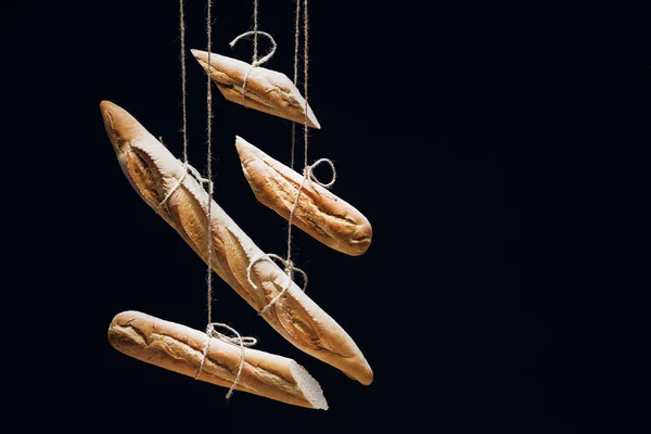 Pagnotte di baguette appena sfornate su corde isolate su nero — Foto stock