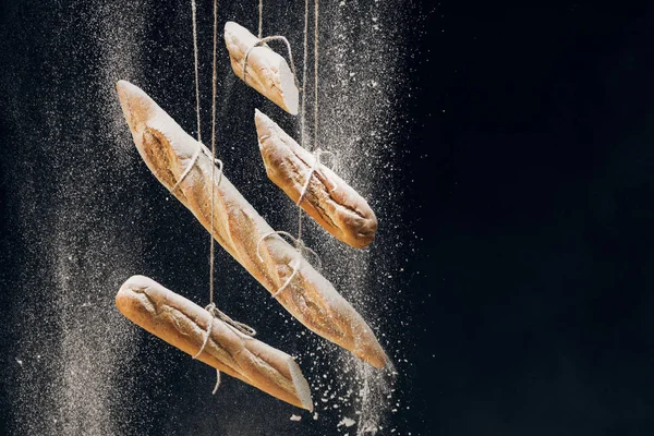 Farine blanche tombant sur des baguettes fraîches cuites au four sur des cordes sur fond noir — Photo de stock