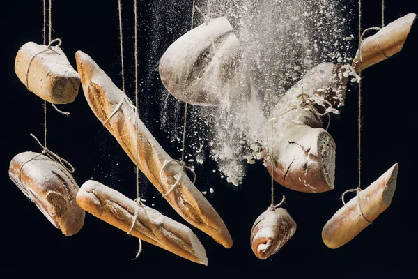 White flour falling at fresh baked bread hanging on ropes on black background — Stock Photo