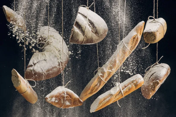Mehl fällt auf frisch gebackenes Brot, das an Seilen auf schwarzem Hintergrund hängt — Stockfoto