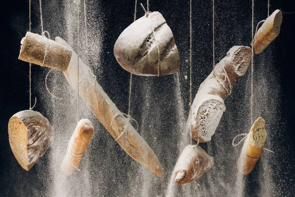 Farine tombant au pain, baguettes et croissant accroché aux cordes sur fond noir — Photo de stock