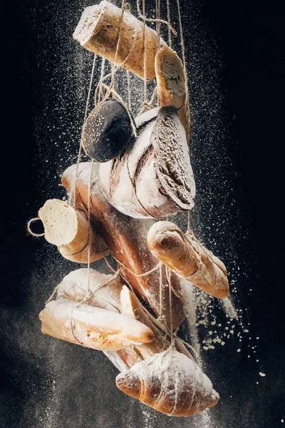 White flour falling at bread, baguettes and croissant on ropes on black background — Stock Photo