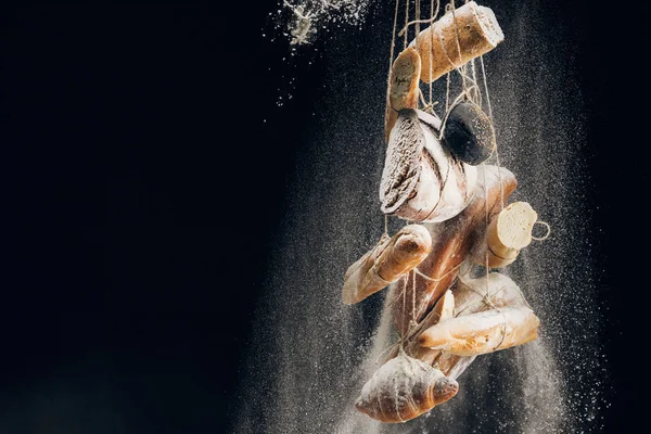 Farinha branca caindo no pão, baguetes e croissant em cordas no fundo preto com espaço de cópia — Fotografia de Stock