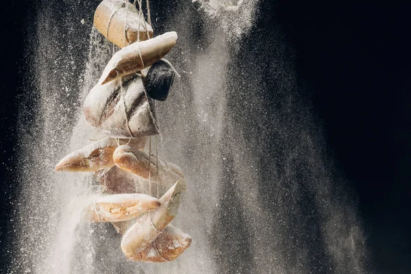 White flour falling at bread and baguettes on ropes on black background — Stock Photo