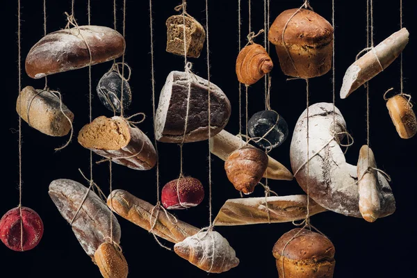 Pães de pão branco e castanho e pastelaria pendurados em cordas isoladas a preto — Fotografia de Stock