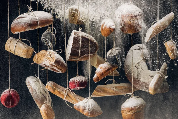 Farinha que cai em pães de pão branco e castanho e pastelaria pendurada em cordas — Fotografia de Stock