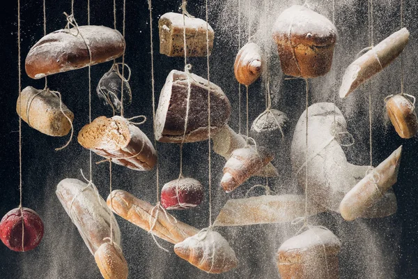 Flour falling at white and brown bread and pastry hanging on ropes — Stock Photo