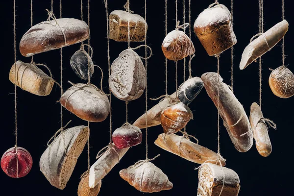 Weißes und braunes Brot und Gebäck hängen an Seilen isoliert auf schwarz — Stockfoto